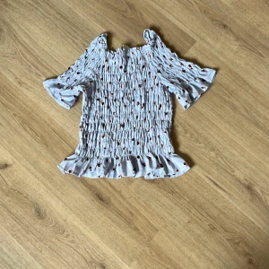 Ljusblå blommig blus med volang - Supersöt ljusblå blus med små rosa och svarta blommor. Smockad över hela kroppen för en tight men stretchig passform och volangkant nertill. Korta ärmar med lätt volang och fyrkantig halsringning. Perfekt för ha på sommaren. Den är från hm men tror inte att den säljs längre. Den är i väldigt bra skick. Den är i storlek 164 men skulle säga att den passar om man har xs/s. Skriv till mig om ni har några frågor. 