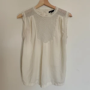 Vit blus med spets från Mango - Vit blus från Mango med transparent spets upptill och broderade detaljer. Ärmlös modell med rund halsringning och lätt, flowy känsla.