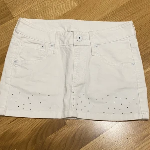 Vit kortkjol med nitar från H&M - Vit jeanskjol från H&M med coola silvriga nitar framtill och på bakfickorna. Klassisk femficksmodell med bälteshällor och knappstängning. Perfekt för dig som gillar en clean men ändå glittrig look.