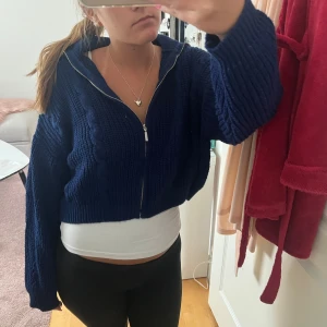 Mörkblå stickad kofta med dragkedja - Säljer en mörkblå stickad kofta med dragkedja framtill. Koftan är croppad och har ett grovt kabelstickat mönster samt långa ärmar. Perfekt för lager-på-lager och chill dagar. Snygg till både jeans och tights.