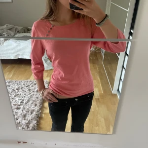 Rosa tröja med knappar vid axeln - Säljer en söt rosa tröja med trekvartsärm och snygga knappar vid ena axeln från märket East. Tröjan har en liten fläck men knappt synlig💗