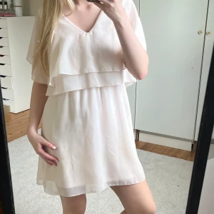 Ljus kortklänning från Vila XS - Supersöt ljus kortklänning från Vila i flowigt material. Klänningen har v-ringning, dubbla lager upptill och korta ärmar. Kan användas åt båda hållen. På bilden har jag den baka och fram då jag tycker det är lite charmigare. Har en defekt/fläck (se bild) som jag ej vet vart det kommit ifrån då den är köpt second hand, och jag har endast använt 1 gång på bröllop. ❤️❤️