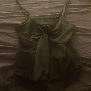 Svart linnetopp med knyt fram - Supersnygg svart linnetopp med justerbara smala axelband och en cool knyt-detalj framtill. Toppen har vågig kant nertill och är perfekt för att skapa en trendig look. Lätt och luftig känsla, passar till många olika outfits.