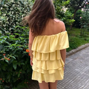 Gul offshoulder volangklänning - Superfin gul kortklänning med flera volanger och offshoulder-modell. Klänningen har en luftig och flowy känsla, perfekt för varma dagar. Den är ärmlös och har en söt, ungdomlig vibe med sin lager-på-lager design.