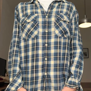 Rutig skjorta från Ralph Lauren M - Snygg flanel skjorta från Denim & Supply Ralph Lauren i blått, beige och svart. Skjortan har två bröstfickor med knappar och klassisk krage. Perfekt för en avslappnad och cool stil.