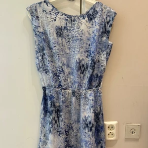 Sommar klänning  - Snygg blåvit med abstrakt och blommigt mönster. Klänningen är ärmlös, har markerad midja och v-ringning framtill. Perfekt för sommarens varma dagar och ger en fräsch och avslappnad look.