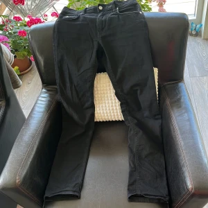 Svarta jeansbyxor från J.Lindeberg - Ett par fina svarta jeansbyxor från J.Lindeberg med klassisk femficksdesign och silverfärgade detaljer. Byxorna har rak passform och är tillverkade i ett mjukt jeanstyg som sitter skönt hela dagen. Perfekta för dig som gillar stilrena plagg, nypris 900kr