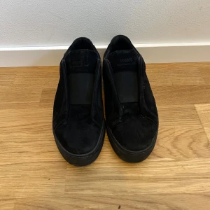 Svarta mockasneakers från Axel Arigato - Stilrena svarta sneakers från Axel Arigato i mjuk mocka med elastiskt band över vristen istället för snörning. Skorna har en platt sula och rund tå, perfekt för en clean och minimalistisk look. Priset går att diskutera vid snabb affär*