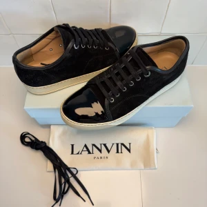 Lanvin skor  - Stilrena svarta sneakers från Lanvin med ovandel i mocka och snygg lackad tå i svart. Skorna har vita sulor, svarta skosnören och klassisk rund tå. Perfekta för dig som gillar en lyxig och clean look med en twist. Obs inget og tillkommer vid köp!! Bara att höra av sig till oss vid minsta fundering😁