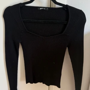 Svart ribbad tröja från Gina Tricot - Snygg svart ribbad tröja från Gina Tricot med lång ärm och fyrkantig ringning. Tröjan har en tight passform och är tillverkad i stretchigt material som sitter skönt på kroppen. Perfekt att styla med jeans eller kjol för en trendig look.