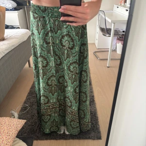 Grön paisleymönstrad långkjol - Supersnygg långkjol från Addictive med paisleyinspirerat mönster i grönt, svart och brunt.. Kjolen har elastisk midja och ett flowy fall som ger en chill och bohemisk vibe. Perfekt för dig som vill sticka ut med coola mönster och färger. Även perfekt nu till sommaren. Jag köpte kjolen i Korsika 2023, men har aldrig använt den. Lappen sitter kvar. Skriv om ni har några frågor. Den har inte någon storlek men passar mig som är 175 med storlek xs/s. 