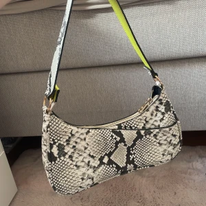 Axelväska i ormmönster från Don Donna - Säljer en snygg axelväska från Don Donna med ormmönster i svart och vitt. Väskan har en bred axelrem med cool limegrön insida och guldfärgad dragkedja. 