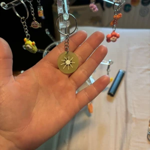 Grön nyckelring med vit stjärndekor - Cool nyckelring med en rund grön bricka och en vit stjärnformad detalj i mitten. Perfekt accessoar att hänga på väskan eller nyckelknippan för en unik touch.