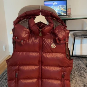 Vinröd dunväst från Moncler - Säljer en vinröd dunväst från Moncler med hög krage och avtagbar huva.