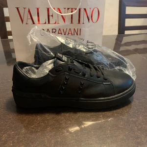 Valentino Rockstud Untitled sneakers svart - Svarta Valentino Garavani Rockstud Untitled sneakers i skinn med ikoniska pyramidnitar ton-i-ton. Klassisk låg modell med snörning och rund tå. Snygg och edgy design som lyfter varje outfit. Sula med rutmönster och logga på insidan. Känns mer som storlek 44