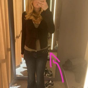 Svart omlottopp med knyt från Gina Tricot - Supersnygg svart omlottopp från Gina Tricot med långa ärmar och stor knytning framtill. Toppen har v-ringning och är gjord i mjukt, stretchigt material som sitter bekvämt. Perfekt för att lyfta vilken outfit som helst. Den är lite nopprig och en tråd sticker ut i ena armen