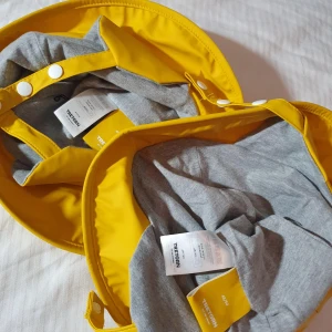 Gul regnhatt från Tretorn - Två coola regnhattar från Tretorn i starkt gul färg med bred brätte och grått innerfoder. Hattarna har tryckknappar vid hakbandet och Tretorn-logga på sidan. Perfekt för regniga dagar när du vill sticka ut.