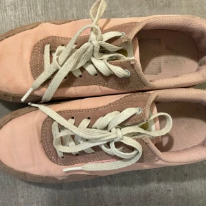 Rosa sneakers från Attitude, strl 37 - Snygga rosa sneakers från Attitude i storlek 37. Skorna har vita snören, detaljer i mocka och textil samt en klassisk rund tå. Perfekta för dig som gillar en sportig och trendig look med en touch av pastell.