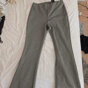 Svarta och vita bootcut byxor H&M - Snygga bootcut byxor från H&M i svartvitt rutigt mönster. Byxorna har hög midja och är i stretchigt material som sitter skönt. Perfekta för dig som gillar en trendig och retro vibe.