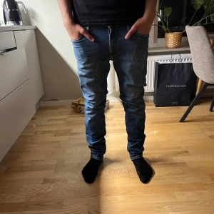Blå jeans Regular Clark Jack & Jones - Säljer ett par blå jeans från Jack & Jones, modell Regular Clark. Normal passform och raka ben. Jeansen är i denim med snygga slitningar och kontrastsömmar. Perfekta för dig som gillar en tidlös och avslappnad stil. Lite slitage. 