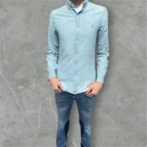 Ljusblå jeans skjorta från Polo Ralph Lauren - Snygg ljusblå skjorta från Polo Ralph Lauren med klassisk button-down krage och broderad logga på bröstet. Skjortan är långärmad, har normal passform och är tillverkad i mjuk bomull. Perfekt för en clean och stilren look. Skjortan har två fläckar ( bild 4, 5 ) men man ser inte dem när man har på sig skjortan nypris: 1600 mitt pris: 119 självklart går det att förhandla ner priset vid snabbköp‼️