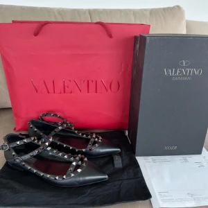 Valentino Rockstud svarta ballerinaskor - Svarta Valentino Rockstud ballerinaskor i skinn med ikoniska nitar i silver. Skorna har spetsig tå, dubbla remmar med spännen och platt sula. Perfekta för dig som vill ha en edgy och lyxig look med statement-detaljer. Använd 1 gång !