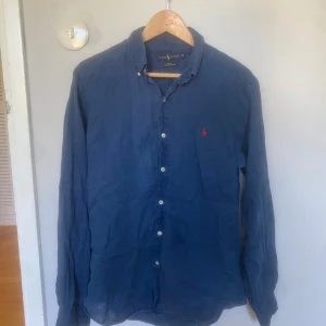 Blå linneskjorta från Ralph Lauren - Snygg blå linneskjorta från Ralph Lauren i slim fit. Skjortan har klassisk krage. Mycket bra skick, storlek M. Hör av er vid intresse!!