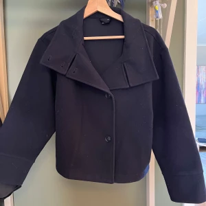 Svart kavaj från Gina Tricot - Marinblå kappa från Gina Tricot i storlek XS. Kappan har en stilren design med knappar framtill och en bred krage. 