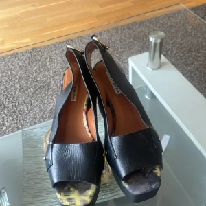 Svarta sandaler med leopardmönster - Snygga svarta sandaler med öppen tå och leopardmönstrad sula. De har en bred rem över foten och en justerbar rem runt hälen. Perfekta för en trendig look.