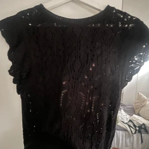 Svart blus - Snygg svart blus med korta ärmar och ett vackert mönster. Perfekt för att lägga till en elegant touch till din outfit. Blusen har en rund halsringning och är lätt och luftig.