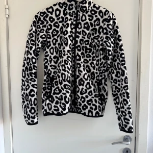 Svartvit leopardmönstrad fleecejacka - Säljer en snygg svartvit leopardmönstrad fleecejacka med dragkedja. Jackan har långa ärmar och är perfekt för att hålla sig varm och stilren. (Katt o kanin finns i hemmet) 