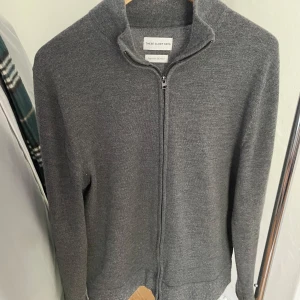 Grå kofta med dragkedja från These Glory Days - Säljer en stilren grå kofta från These Glory Days. Den har en praktisk dragkedja framtill och är tillverkad i ett mjukt material. Perfekt för lager-på-lager under kyligare dagar.