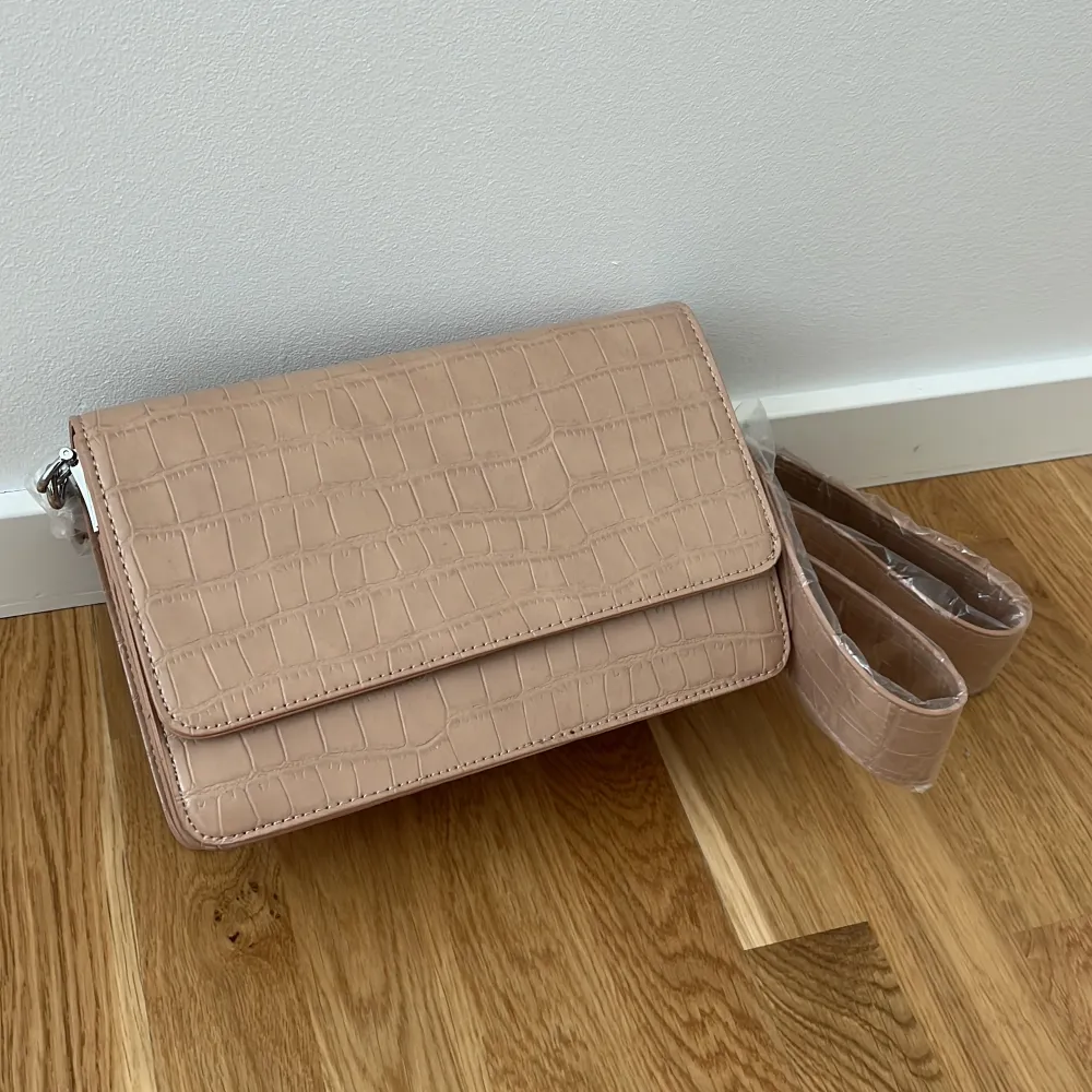 Snygg beige axelväska med krokodilmönster och justerbar axelrem. Väskan har en praktisk dragkedja inuti för säker förvaring. Perfekt för att ge din outfit en stilfull touch.. Laukut & Käsilaukut.