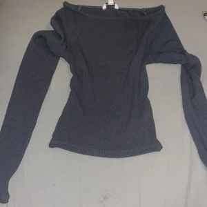 Mörkgrå offshoulder topp från Clockhouse - Säljer en stilren mörkgrå offshoulder topp från Clockhouse. Toppen är ribbad och har långa ärmar, perfekt för en trendig look. Passar bra till både jeans och kjol. Perfekt för dig som vill ha något enkelt men snyggt i garderoben.