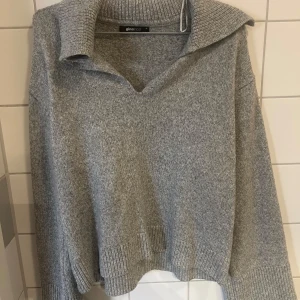 Grå stickad tröja från Gina Tricot - Mysig grå stickad tröja från Gina Tricot med en avslappnad passform. Tröjan har en v-ringad krage och långa ärmar med ribbade muddar. 