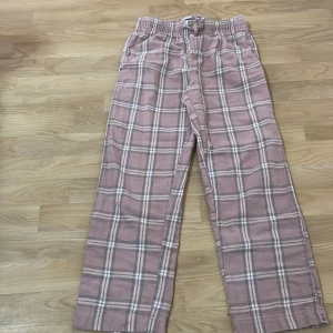 Rosa rutiga byxor med resårmidja - Säljer ett par bekväma rosa byxor med rutigt mönster och resårmidja. Byxorna har en avslappnad passform och är perfekta för en ledig stil. De har även en praktisk snörning i midjan för justerbar passform.