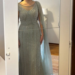 Glittrig festklänning  - Säljer min vackra klänning för 2500 kr, endast använd en gång. Då jag bytte klänning halvvägs under bröllopet, är den i mycket fint skick. Klänningen är kortad för att passa mig som är 163 cm lång med klackar. Storlek UK 10, vilket motsvarar EU 40. Exakta mått finns i bilderna. Köparen står för frakten