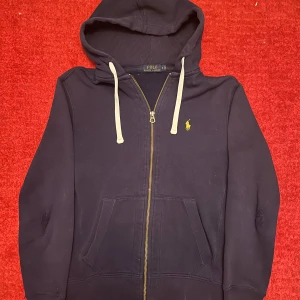 Ralph lauren tröja - Säljer denna snygga Ralph lauren zip tröjan i den populära färgen marinblå  för ett riktigt bra pris. Tröjan är i använt skick med lagade defekter (se bilder) men har mycket kvar att ge. Utöver bilderna är tröja i ett bra skick. Vid frågor eller fler bilder är det bara att fråga.