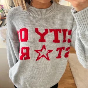 Grå stickad tröja med röd text - Säljer en grå stickad tröja med röd text (city of stars) och stjärndetalj på framsidan.💋🌟