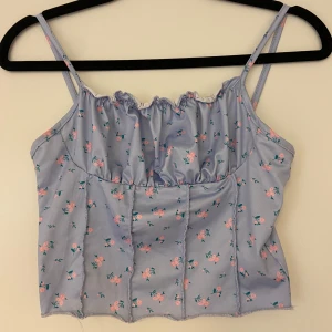 Ljusblå blommig linnetopp - Söt lila linne med rosa blommor och smala axelband. Toppen har en rynkad detalj vid halsringningen.