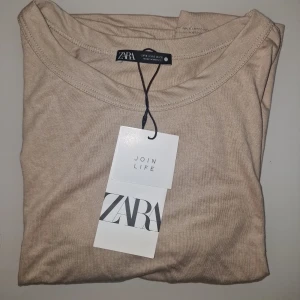 Beige t-shirt från Zara - Säljer en stilren beige t-shirt från Zara. Perfekt för en enkel och avslappnad look. Den är lätt att matcha med det mesta och är ett  bra basplagg i garderoben.