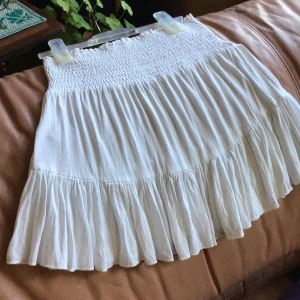 Vit kjol med volangdetaljer - Charmig vit kjol med volangdetaljer och elastisk midja. Perfekt för en somrig look. Kjolen har en luftig och bekväm passform som gör den idealisk för varma dagar.