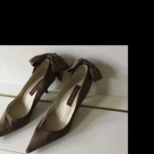 Bruna pumps med rosett från Renata Mucci - Eleganta bruna pumps från Renata Mucci med en stor dekorativ rosett på baksidan. Skorna har en spetsig tå och är tillverkade i ett glansigt material som ger en lyxig känsla.