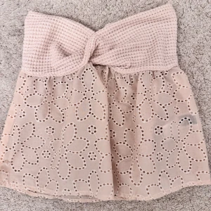 Beige sommar topp med spetsdetaljer - Söt beige tröja med en stickad tubtopp och vackra spetsdetaljer i blommönster. Perfekt för en somrig look. Tröjan har en kort längd och en elastisk passform som gör den bekväm att bära.