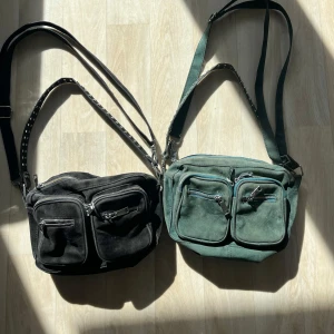 Svart och grön axelväska i mocka - Två snygga noella väskor i mocka, en i svart och en i grön. Båda har flera praktiska dragkedjefickor framtill och justerbara axelremmar med nitar. Nypris på än är runt 400-500. Köp en för 200 eller båda för 390. Väskorna är använda så kom privat för bilder på slitningar. 