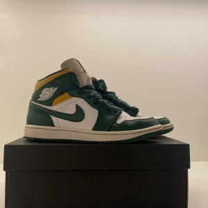 Nike Air Jordans 1 Mid i grönt och vitt - Snygga Nike Air Jordans i en fräsch kombination av grönt, vitt och gult. Skorna har den klassiska höga designen med snörning och en robust sula. Perfekta för dig som vill ha en stilren och sportig look.