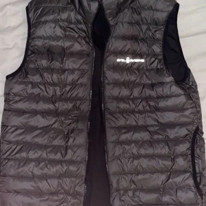 Svart reversable sail racing väst - Snygg svart dunväst från sail racing med dragkedja framtill. Västen har en vanlig dun sida och en gortex sida. Den har en stilren look och är lätt att matcha med olika outfits.