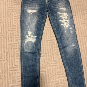 Blå jeans från Dondup - Snygga blå jeans från Dondup med slitna detaljer och en klassisk femficksdesign. De har en normal passform och är perfekta för en avslappnad stil. Märkeslappen i brunt läder ger en extra touch.
