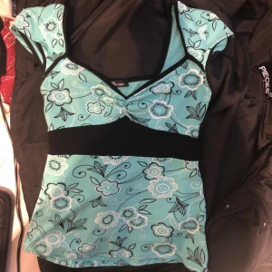 Jätte gullig tooo - Säljer en söt turkos topp med blommigt mönster från . Toppen har en v-ringad design och korta ärmar med en svart detalj under bysten som man kan knyta för en tight look.  Perfekt för en somrig look!