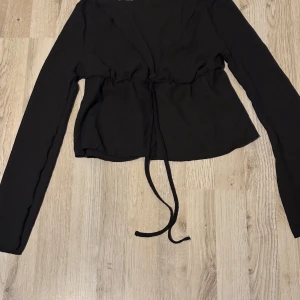 Svart långärmad topp med knyt - Snygg svart långärmad topp med knyt i midjan för en justerbar passform. Perfekt för en stilren look.